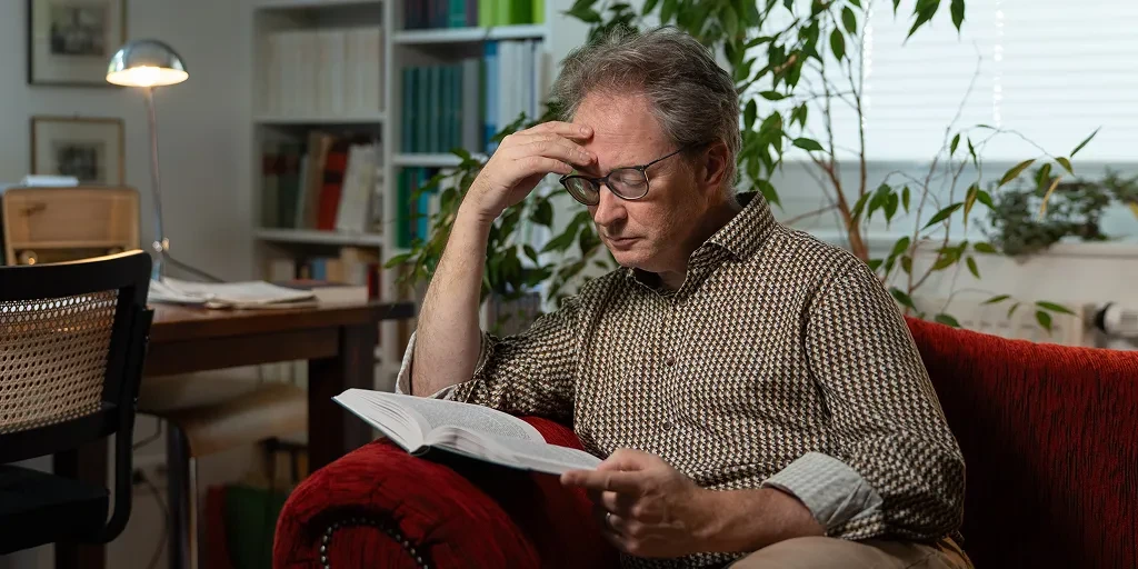 Wilm Hüffer sitzt auf einem roten Sofa und liest in einem Buch